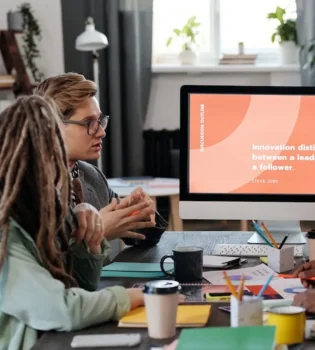 3 people sitting at a table with a computer screen, meticulously discussing a business proposal.