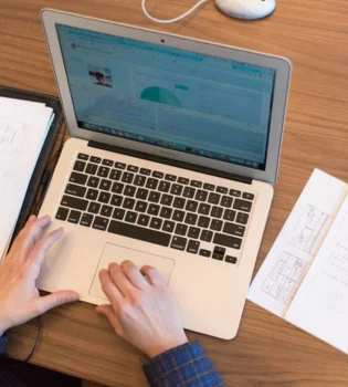 A man uses his laptop to create PowerPoint slides implies the ppt presentation services in India.