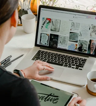 A woman quickly doing product descriptions content writing on her laptop with a pen and tablet.