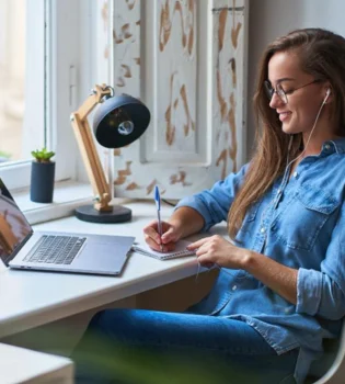 A woman seated at a desk with a headphones, working on her computer for speech writing services.