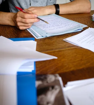 A person working on term papers writing while seated at a table with pens and paper.