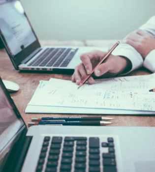 A person developing user manual content services while using a laptop along with pen and paper.