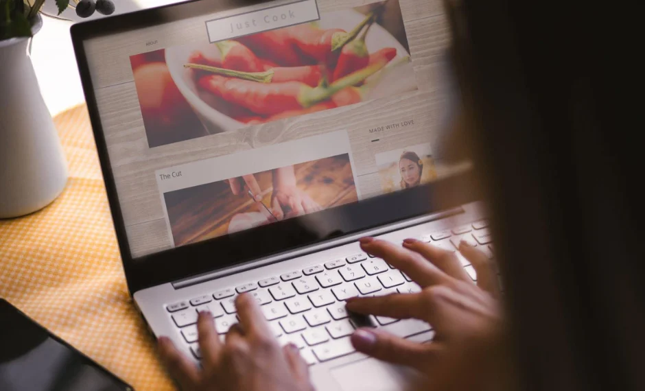 A woman typing on a laptop with a picture of food on it is working as a content builder.